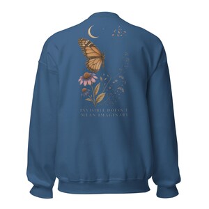 May include: A dark blue crewneck sweatshirt featuring a back graphic of a monarch butterfly, a crescent moon, and purple flowers. The text "INVISIBLE DOESN'T MEAN IMAGINARY" is printed in a light font below the floral and butterfly illustration.