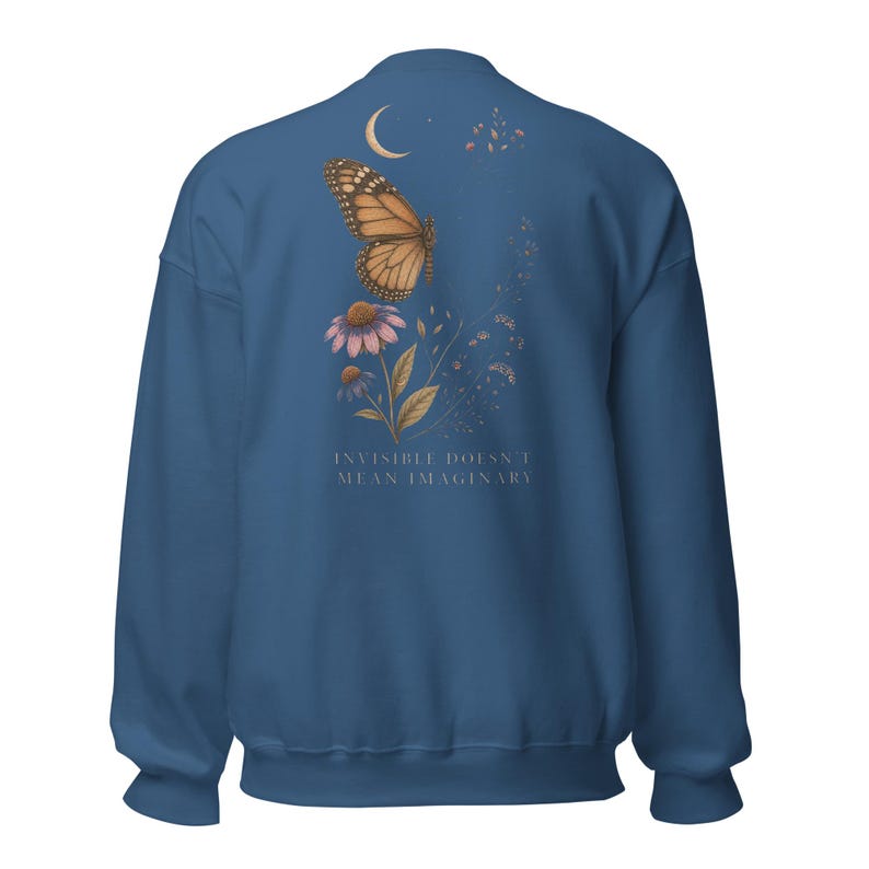 May include: A dark blue crewneck sweatshirt featuring a back graphic of a monarch butterfly, a crescent moon, and purple flowers. The text "INVISIBLE DOESN'T MEAN IMAGINARY" is printed in a light font below the floral and butterfly illustration.