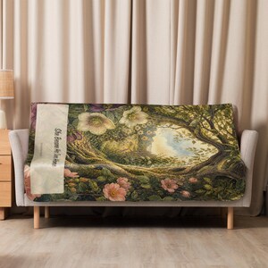 May include: A rectangular throw blanket featuring a detailed illustration of a lush forest scene with large pink and white flowers, twisted tree branches, and green foliage. A vertical cream-colored panel displays the text She Became Her Own Home.