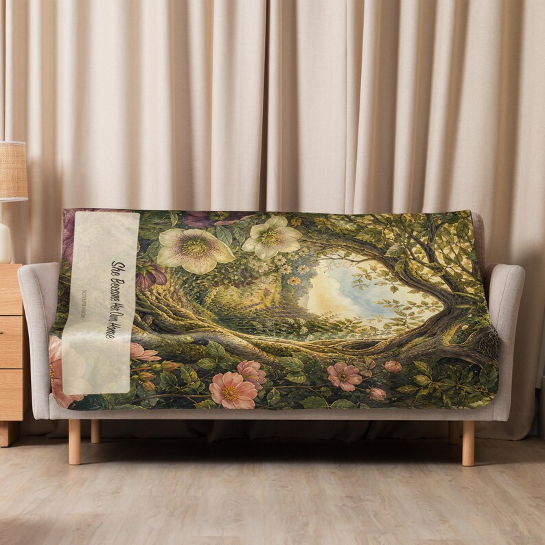 May include: A rectangular throw blanket featuring a detailed illustration of a lush forest scene with large pink and white flowers, twisted tree branches, and green foliage. A vertical cream-colored panel displays the text She Became Her Own Home.