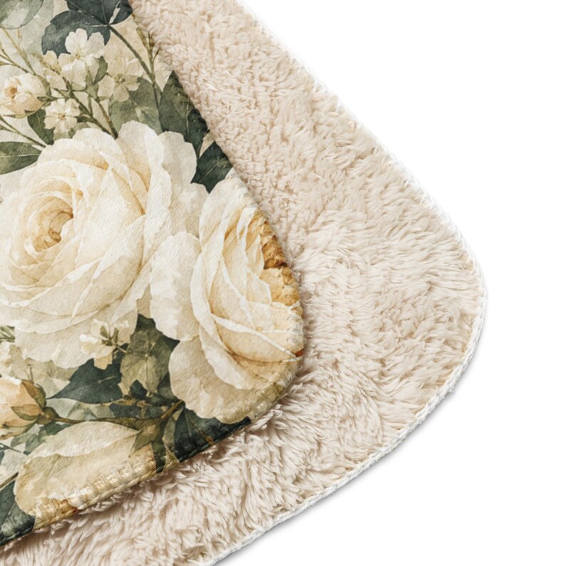 May include: A plush throw blanket featuring a detailed floral print of large cream-colored roses and dark green foliage on one side, with a thick, textured, beige sherpa fleece lining on the reverse side, showcasing the soft, fuzzy fabric edge.