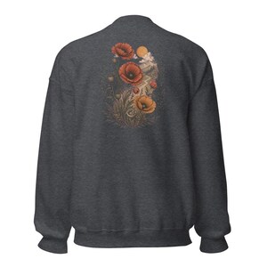 May include: A charcoal gray long-sleeve sweatshirt featuring a graphic on the back. The design displays red and orange poppy flowers, foliage, and a small sun set against a landscape with a winding path, rendered in muted, earthy tones.