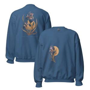 May include: A blue crewneck sweatshirt featuring a graphic of a dark purple iris flower with golden yellow leaves and a circular moon-like shape. The back of the sweatshirt displays a larger version of the same floral design with text below it.
