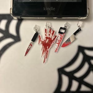 May include: Four Halloween-themed charms, including a bloody hand, a bloody knife, a bloody saw, and a bloody knife. The charms are made of clear plastic with red and black paint.