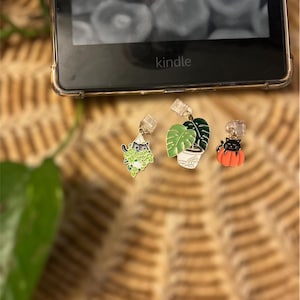 May include: Three gold-colored cat-themed bookmarks with clear plastic clips. The bookmarks feature a black cat in a hanging plant, a black cat in a potted plant, and a black cat in a pumpkin.
