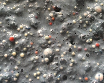May include: Close-up of a blue slime with white, orange, and black beads mixed in. The slime has a textured surface and appears to be very thick.