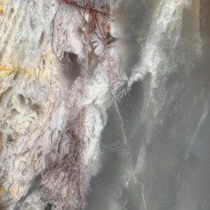 May include: Abstract close-up of a stone surface with a mix of colors. The stone features areas of white, gray, and brown, with intricate patterns and textures. The overall appearance is smooth and polished.