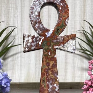 May include: A brown, white, and green agate Ankh, a symbol of life and eternal life in ancient Egypt. The Ankh is a cross with a loop at the top.