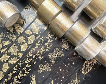 May include: Decorative washi tape rolls and patterned strips. The rolls are gold and silver. The strips are black with gold botanical and celestial designs, including leaves, butterflies, and stars. Perfect for scrapbooking and crafts.