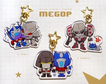 May include: Clear acrylic keychains featuring cartoon versions of Transformers characters. Each keychain has a gold star-shaped clasp. The keychains include characters like Optimus Prime and Megatron, with the text "ALISA AYDIN / CHARM" and "MEGOP".