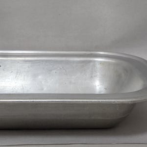 May include: A rectangular aluminium baking pan with rounded corners and a wide rim. Next to the pan is a small red and white matchbox with the text Redheads 45 safety matches and an illustration of a person with red hair on the front.