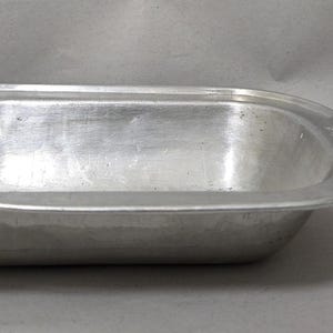 May include: An oval-shaped silver-coloured metal baking pan with a wide rim. Next to the pan is a small rectangular box of Redheads 45 safety matches, which provides a visual scale reference for the size of the metal container.