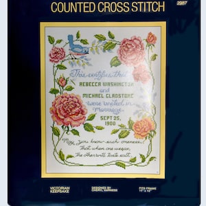 May include: A counted cross stitch pattern featuring a wedding certificate with pink roses and a blue bird. The text reads "This certifies that Rebecca Washington and Michael Gladstone were united in marriage Sept 25, 1900. May you know such oneness, that when one weeps, the other will taste salt." The pattern is designed by Cheryl Harness and fits a 11 x 14 inch frame.