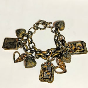 May include: A gold-toned charm bracelet with a chain link design and multiple charms, including hearts, a small square, and a rectangular charm with the word "LOVE" inscribed on it.