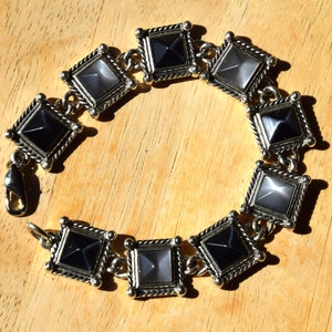 May include: A silver bracelet with alternating black and white square-shaped stones. The stones have a pyramid-like design.