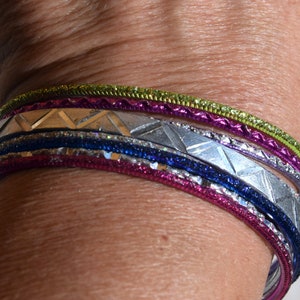 May include: A set of five colorful bracelets with a silver, patterned bracelet in the center. The bracelets are stacked on a person's wrist.