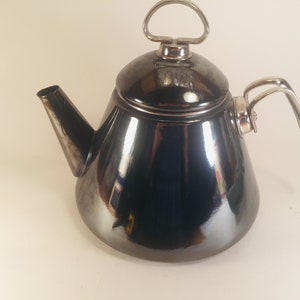 May include: A black metal teapot with a silver handle and lid. The teapot has a shiny, reflective finish.