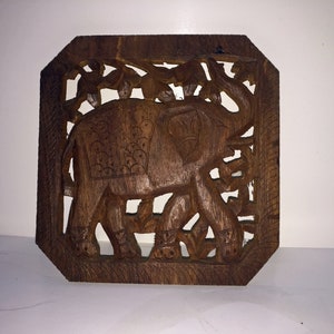 May include: A dark brown wooden wall hanging featuring an intricately carved elephant design surrounded by foliage.