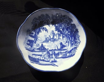 May include: A white ceramic bowl with a blue and white design of a castle and trees. The bowl has a scalloped edge.