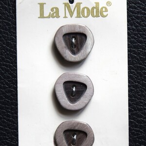 May include: A pack of three brown and white buttons with a triangular design. The buttons are labeled "La Mode" with a registered trademark symbol.