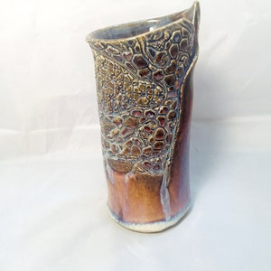May include: A brown ceramic vase with a textured, geometric design. The vase has a slightly irregular shape and a white glaze on the bottom.