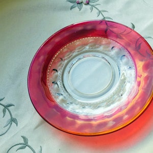 May include: A clear glass saucer with a decorative rim and a red and orange iridescent finish.