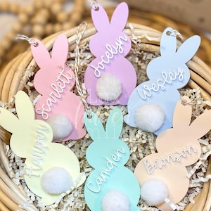 May include: Six pastel colored bunny shaped Easter tags with white pom pom tails. The tags are decorated with names: Harper, Camden, Bronson, Jocelyn, Wesley, and Scarlett.
