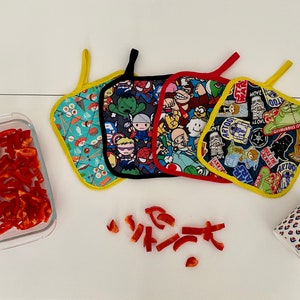 Può includere: Quattro presine colorate con diversi disegni di personaggi dei cartoni animati. Le presine sono fatte di tessuto e hanno un bordo giallo.