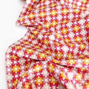 May include: A white fabric with a repeating pattern of pink, orange, and yellow overlapping circles forming star shapes.