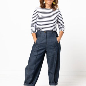May include: A woman wearing a white and navy striped long-sleeve shirt, dark blue denim jeans with pleats, and black and white sneakers.