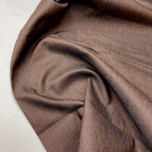 May include: Close-up of a brown fabric with a subtle textured pattern. The fabric is soft and smooth, with a slight sheen.
