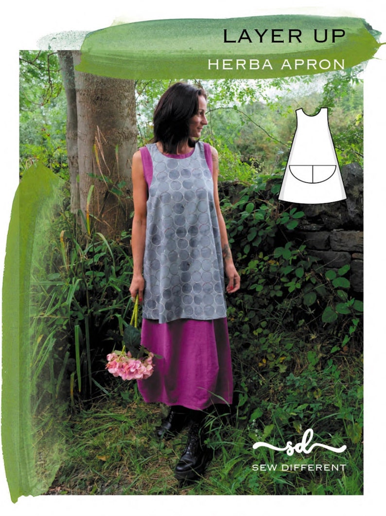 Puede incluir: Una mujer lleva un delantal sin mangas de estampado gris y blanco sobre un vestido rosa, de pie en un jard&iacute;n sosteniendo un ramo de flores rosas. El delantal se llama "Herba Apron" y forma parte de la colecci&oacute;n "Layer Up". El texto "Sew Different" tambi&eacute;n es visible en la imagen.