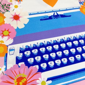 May include: A colorful, floral-themed fabric featuring a typewriter design. The typewriter has a blue keyboard with white keys and letters. A sheet of paper with an orange heart is above the keyboard. Pink, orange, and white flowers surround the typewriter.