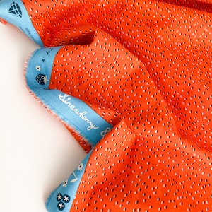 May include: Orange fabric with a white polka dot pattern. The fabric has a blue border with the text "Strawberry &" printed on it.