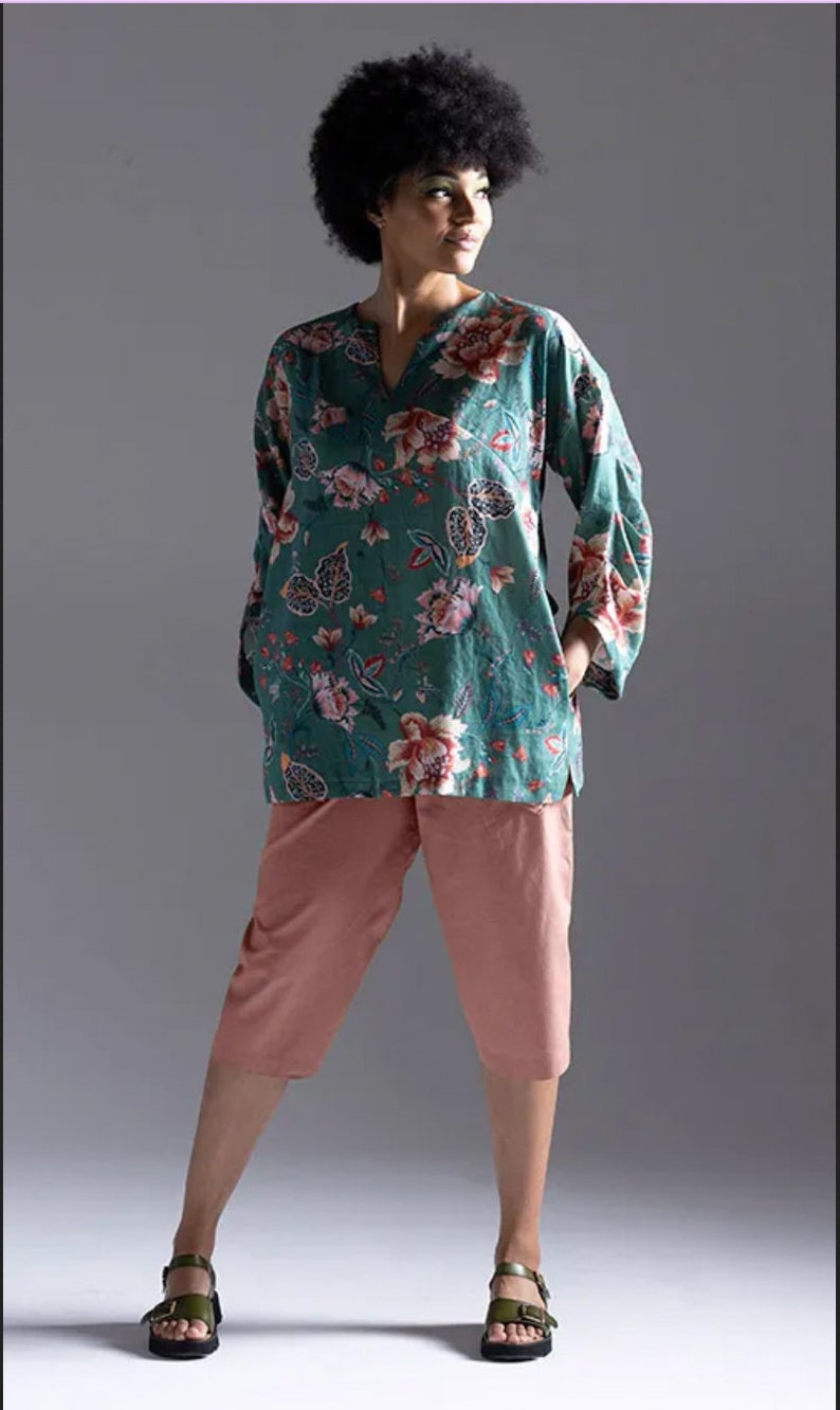 May include: A woman wearing a teal floral print top with a v-neck and long sleeves. She is also wearing pink cropped trousers and green sandals.