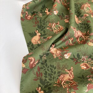 May include: Green fabric with a repeating pattern of woodland animals, including deer, rabbits, and squirrels, amidst foliage. The design features shades of brown and tan against a green background, creating a nature-inspired theme.