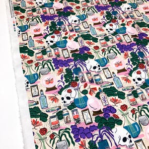May include: A cream-coloured fabric with a repeating pattern of skulls, butterflies, plants, and glass bottles. The pattern is in shades of pink, blue, green, and purple.