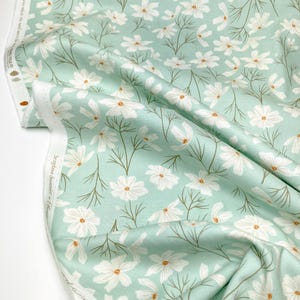May include: A light blue fabric with a white floral pattern. The fabric features a repeating pattern of white cosmos flowers with brown centers and green stems.