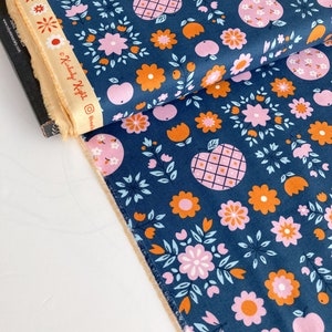 May include: A blue fabric with a repeating pattern of pink and orange flowers, apples, and leaves. The fabric has a white border.