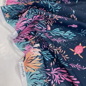 May include: A dark blue fabric with a repeating pattern of coral, seaweed, fish, and sea turtles. The fabric has a watercolour-like effect and is printed with the text "©  Shona Knight".