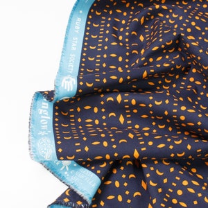 May include: A navy blue fabric with a repeating pattern of orange geometric shapes, including circles, crescents, and diamonds. The fabric has a blue and white border with the text "RUBY STAR SOCIETY" and "nglow".