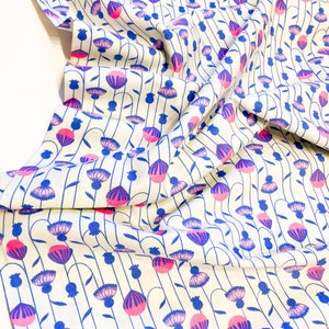 May include: White fabric with a repeating pattern of pink and blue flowers. The flowers are stylized and have a simple design. The fabric is folded and draped.