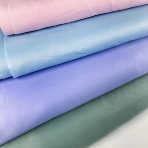 May include: A close-up of fabric swatches in pastel shades. The colours are light pink, light blue, lavender, and sage green. The material appears to be smooth, possibly satin or silk.