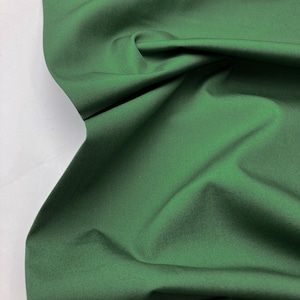 May include: A close-up of a deep green fabric with a smooth texture. The fabric is folded and draped, showing its soft and flowing nature.