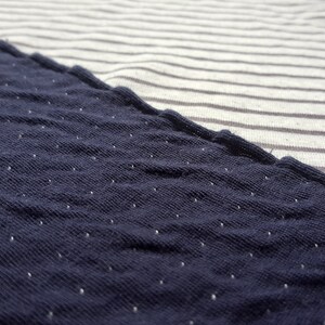 May include: Close-up of a navy blue fabric with white polka dots. The fabric is textured and has a slightly rough feel.