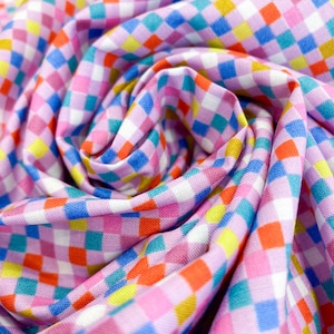 May include: A close-up shot of a fabric with a vibrant checkered design. The fabric displays a repeating pattern of small squares in pink, blue, orange, yellow, and white. The fabric is gathered and folded, creating a swirling effect.