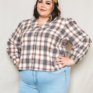 May include: A woman wearing a white and brown checked long-sleeved button-up shirt with a collared neckline and blue jeans.