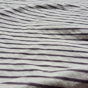 May include: Close-up of a white and gray striped fabric with a subtle texture. The fabric is wrinkled and has a soft, casual look.