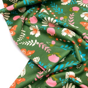 May include: Green fabric with a floral pattern featuring pink and white flowers, butterflies, and leaves. The fabric has a subtle sheen and a soft texture.