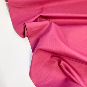 Peut inclure: Un gros plan sur un tissu rose foncé à la texture lisse. Le tissu est plié et drapé, mettant en valeur sa douceur et sa fluidité.